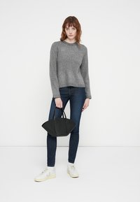 Grå strikkegenser med rund hals, parret med mørke jeans og hvite joggesko, holder en svart håndveske. Enkel og moderne design.