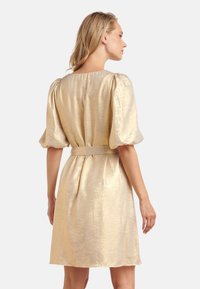 Kurzärmliges, goldenes Kleid mit strukturierter Oberfläche, tailliertem Oberteil und glockigem Rock. Inklusive passendem Gürtel in der Taille.