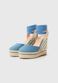 Modré denimové espadrilky na wedges se tkanými juty, s vrstvovým designem a zkříženými kotníkovými popruhy z odpovídající modré látky.