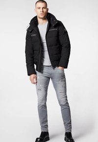 Czarna kurtka puchowa z kapturem, z zamykanymi kieszeniami z przodu i teksturowanym wykończeniem, w połączeniu z jasnoszarymi dżinsami z przetarciami i czarnymi botkami za kostkę.