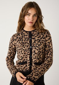 Cardigan en imprimé léopard beige et noir, avec une fermeture à boutons, des finitions noires et deux poches ; matériau tricoté à la texture douce.