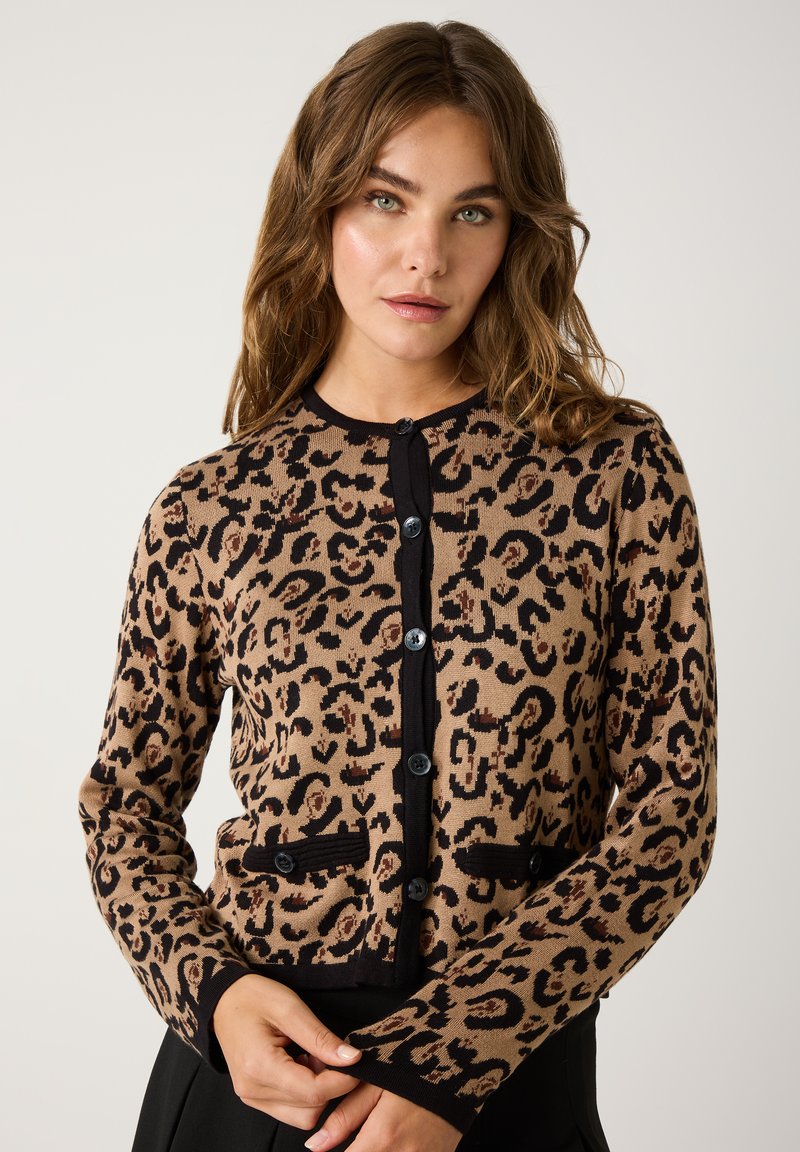 Cardigan en imprimé léopard beige et noir, avec une fermeture à boutons, des finitions noires et deux poches ; matériau tricoté à la texture douce.