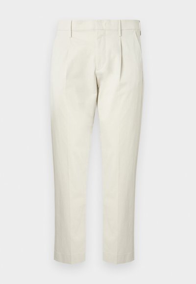Pantalon beige sur mesure avec passants de ceinture, plis avant, poches latérales et jambes droites, présenté sur un fond uni.