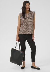 Braun gemusterte Bluse mit kurzen Rüschensäumen, kombiniert mit schwarzen Slim-Pants und einer schwarzen Ledertasche. Schwarze Ballerinas runden das Outfit ab.