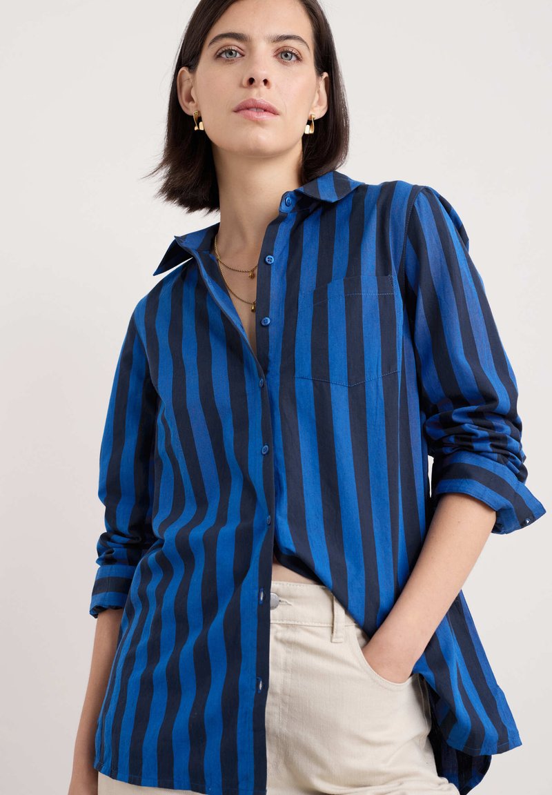 Camicia a strisce blu con audaci strisce verticali di varie tonalità, davanti con bottoni, colletto e una tasca sul petto.