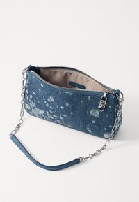 Sac à main en denim avec un motif éclaboussé bleu, bandoulière en chaîne argentée et fermeture éclair. L'intérieur présente une doublure de couleur claire.
