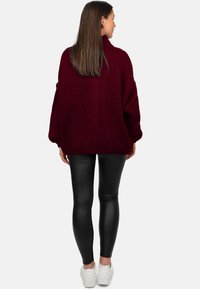 Pull en grosse maille bordeaux avec col montant, poignets et ourlet côtelés, associé à des leggings noirs brillants et des baskets blanches.