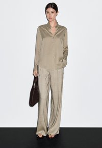 Lichtolijfgroene satijnen blouse met een kraag, gecombineerd met beige geruite wijde broekspijpen en een donkerbruine totebag.