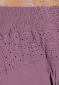 Lila idrottsshorts med en texturerad midjeband, perforerad panel för andningsförmåga och en slät tygfinish.