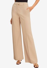 Beige weite Hosen aus glattem Stoff mit hoher Taille, vorderen Falten und seitlichen Taschen, kombiniert mit schwarzen Absatzsandalen.