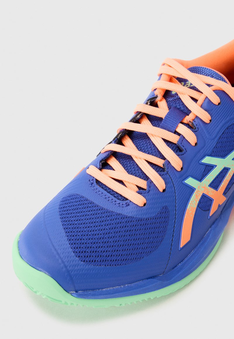 Blå sportssko med mesh-materiale, orange snørebånd, grøn sål, unik logo detalje og strømlinet design. Rund tå og teksturerede detaljer.