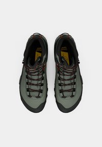 Roheline matkasaapad mustade taldade, punaste detailide ja vastupidava materjaliga. Omab kõrget disaini tugevdatud nööpide ja tekstureeritud pinnaga.