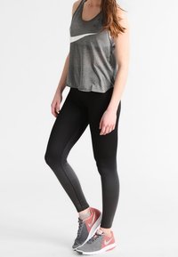 Grijze sportieve tanktop met wit logo, zwarte textuurtights en grijs-roze hardloopschoenen met een bovenkant van mesh en contrasterende accenten.