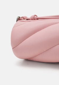 Vaaleanpunainen nahkalaukku, jossa on tikattu muotoilu diagonaalisella ompelulla, pyöreä muoto ja ohut hihna. Koristeina metalliset varusteet.