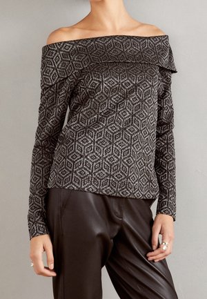 Haut à manches longues épaules dénudées avec motif géométrique noir et argenté, associé à un pantalon en cuir noir taille haute.