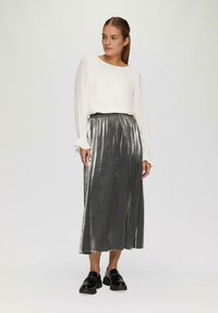 Witte blouse met geplooide lange mouwen, gecombineerd met een metallic zilveren maxi-rok. De outfit heeft een hoge taille en een gladde textuur.