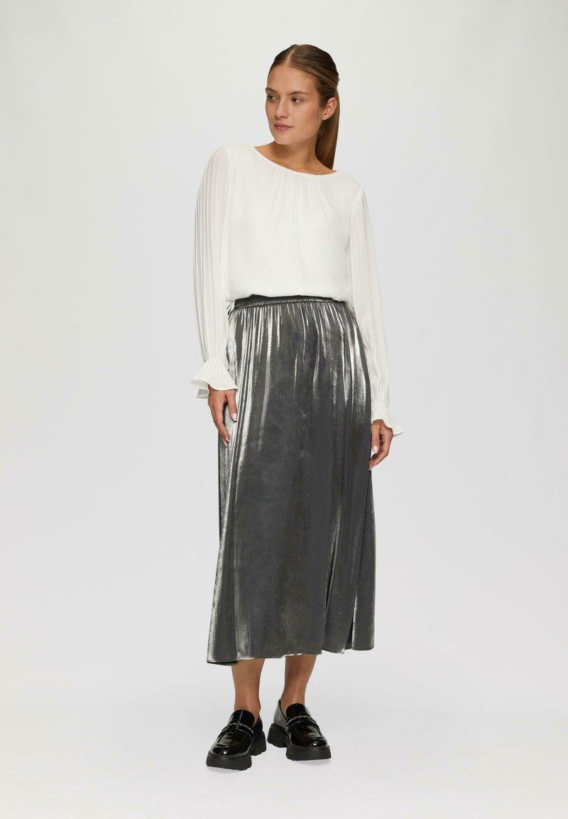 Witte blouse met geplooide lange mouwen, gecombineerd met een metallic zilveren maxi-rok. De outfit heeft een hoge taille en een gladde textuur.