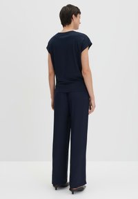 Top blu navy a vestibilità rilassata con maniche arrotolate, abbinato a pantaloni blu navy dal taglio morbido. Design semplice con tessuto leggero e liscio.