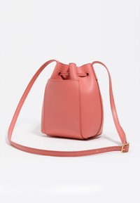 Różowa skórzana torba typu bucket z zaokrągloną podstawą, z zamknięciem na sznurek i regulowanym paskiem. Gładka faktura, minimalistyczny design i jedna boczna kieszeń.