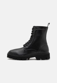 Bottes en cuir noir à lacets avec un bout arrondi, surface texturée, semelle en caoutchouc robuste et une tirette à l'arrière pour un enfilage facile.