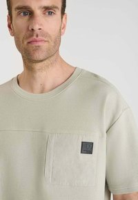 Lichtgroene, gestructureerde, korte mouwen shirt met een borstzak en een zwart logo-patch, met een ronde halslijn en een ontspannen pasvorm.