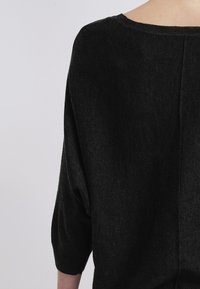 Maglione nero dal taglio ampio realizzato in un morbido tessuto a maglia. Presenta maniche a tre quarti e un ampio scollo con una cucitura centrale.