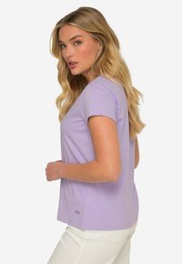 T-shirt violet clair à manches courtes avec une coupe décontractée, texture lisse et un petit accent de logo en bas. Design simple et polyvalent.