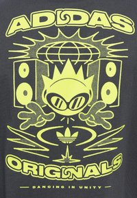 Pogumna rumena grafika na črni podlagi, ki prikazuje stiliziranega lik s krono in očali, zvočnike, globus, logo Adidas ter besedilo "ADIDAS ORIGINALS" in "PLES V ENOTI".