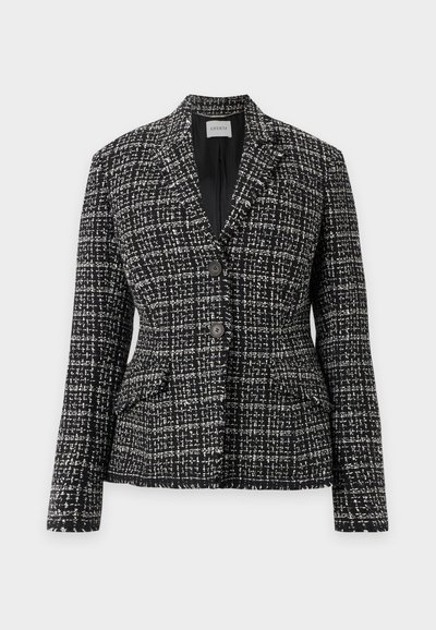 Blazer femme en tweed noir et blanc avec deux boutons sur le devant, col à revers cranté et deux poches à rabat sur fond clair.