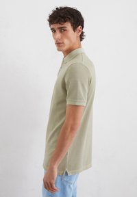 Lichtgroene polo met korte mouwen, voorzien van een kraag en knoopsluiting, gedragen met blauwe denim jeans.