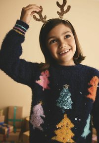 Granatowy, puszysty sweter z kolorowymi aplikacjami przedstawiającymi różowe, pomarańczowe i żółte drzewa; posiada błyszczące poroże noszone na głowie.