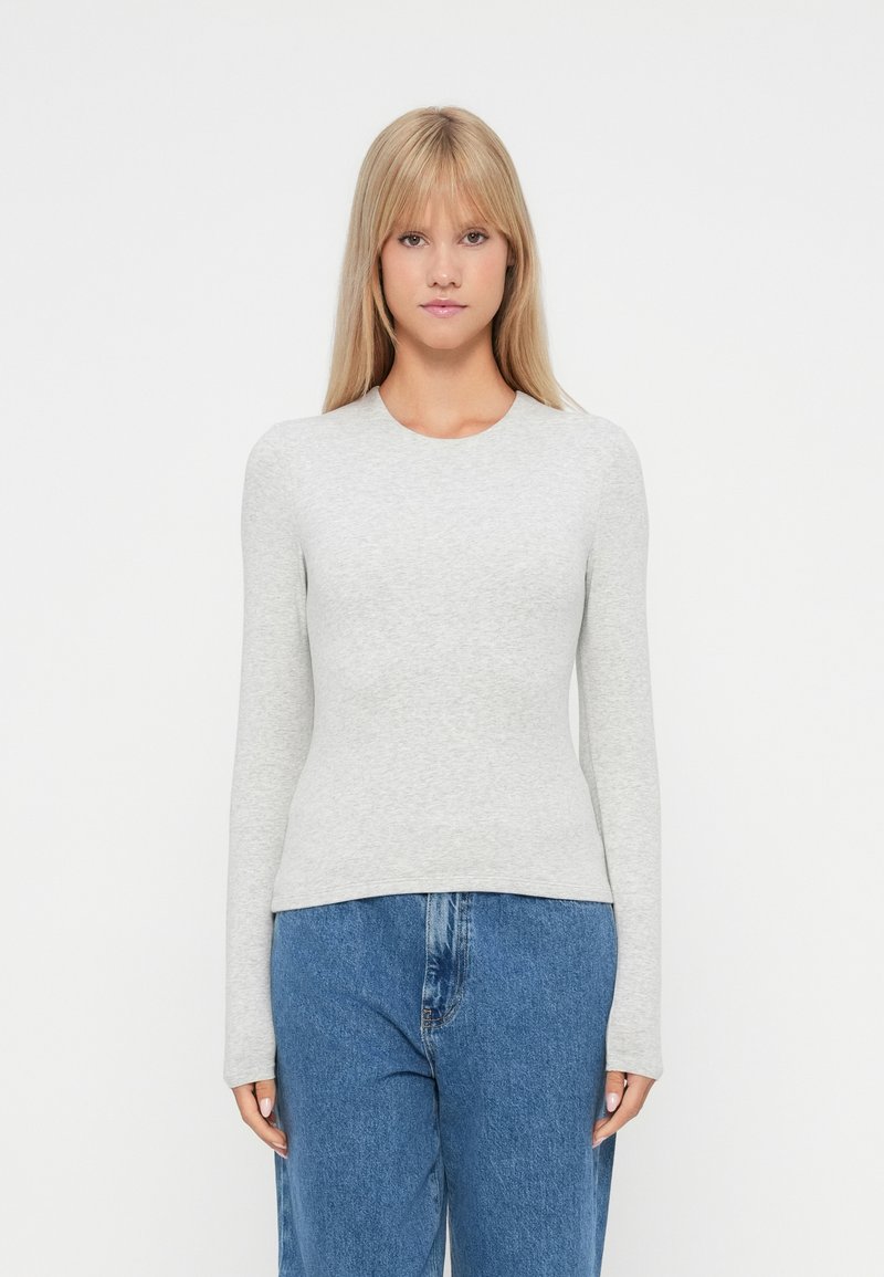 Langærmet grå top lavet af blødt stof, med rund halsudskæring og tætsiddende design, parret med løse blå jeans.
