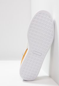 Vit sneaker sula med texturerat grepp, med en framträdande svart logotyp, ljusgrå övre material och en antydan av orange på sidorna.
