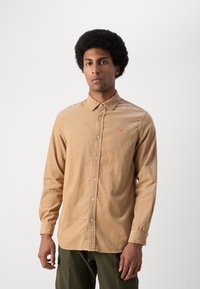 Camisa de manga larga, con botones, hecha de suave tela beige, que presenta un pequeño logo rojo en el pecho y un diseño de cuello clásico.