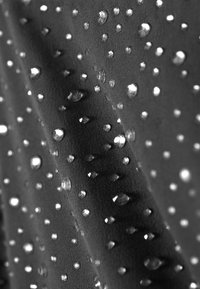 Textília s tmavým základom, s vystúpenými, lesklými kvapkami usporiadanými do rozptýleného vzoru, ktoré zvyšujú textúru a vizuálny záujem.