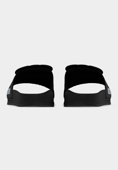 Paire de sandales noires à enfiler avec des brides larges et un texte blanc sur le côté, vue de dos sur un fond blanc uni.