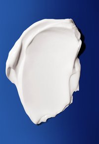 Hvid fløde spredt ud over en glat blå baggrund, med en glossy finish og uregelmæssige, flydende kanter. Ingen synlige mønstre eller accenter.