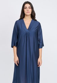 Marineblaues, knielanges Kleid aus glattem Stoff mit V-Ausschnitt und 3/4-Ärmeln in Glockenform, das in der Mitte vorne eine Raffung aufweist.