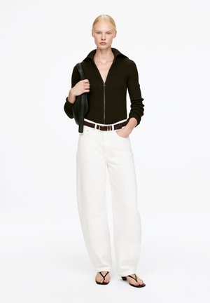 Dark brown zip-up ribbed sweater, white wide-leg trousers, black belt, and black flip-flops. Minimalist design with a sleek look.