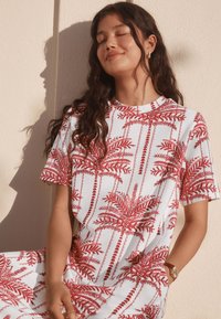 Korte mouwen jurk in wit met rode tropische palmbladprint, voorzien van een ronde halslijn en een losse pasvorm. Gladde stof met een zachte textuur.