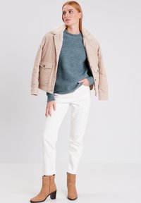 Beige corduroy jasje met een nep bontkraag, getextureerde teal trui, witte broek en tan hoge hakken. Focus op casual, gelaagde stijl.