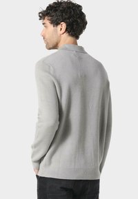 Grå strikkegenser med sjalkrage og lange ermer. Myk tekstur og avslappet passform, med ribbestrikket kant og mansjetter.