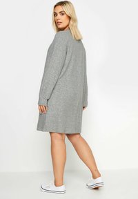 Abito a maglia grigia a coste con maniche lunghe e scollatura rotonda, progettato per arrivare a metà coscia. Abbinato a sneakers bianche.