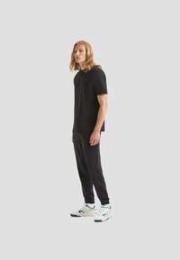 T-shirt nera a maniche corte e pantaloni jogger abbinati, entrambi realizzati in tessuto morbido. Sneakers bianche con dettagli verdi completano l'outfit.