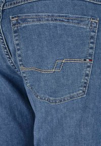 Spijkerbroek met een achterzak met contrasterende stiksel in een zigzagpatroon. Het materiaal is een lichtblauwe denim met een subtiele textuur.