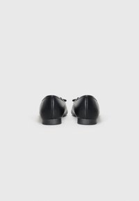 Mocasini din piele neagră, cu vârf rotund, tocul mic și detalii decorative sub formă de fundiță în față. Textură netedă.