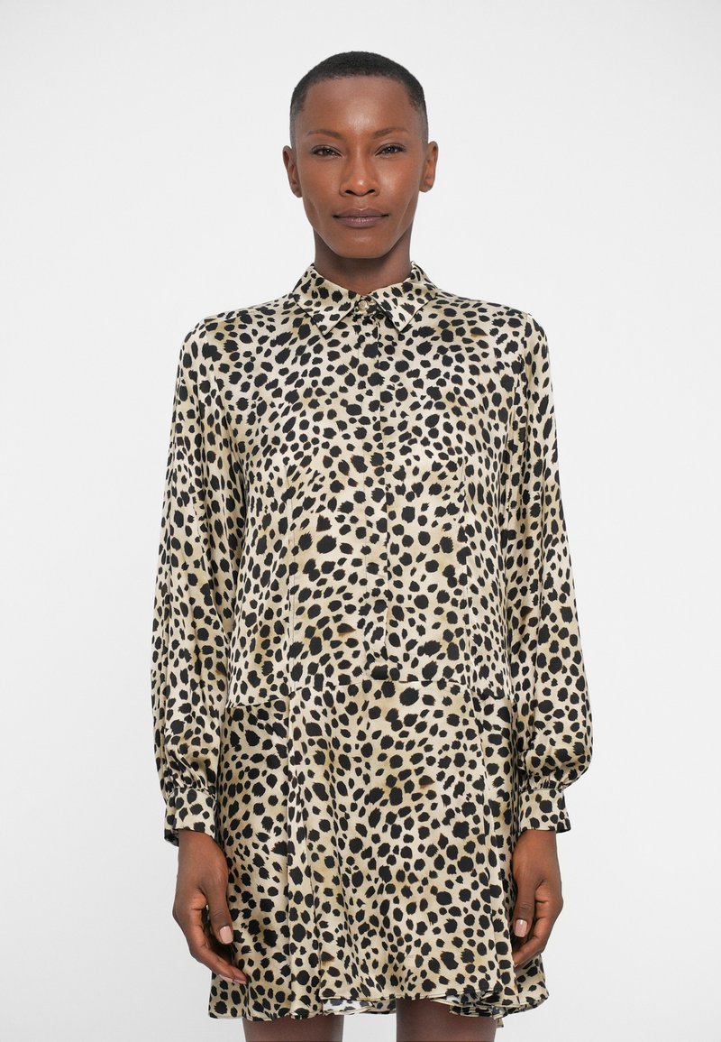 Vestido camisetón de estampado de leopardo en beige claro y negro, con un diseño de botones, mangas largas y un ajuste relajado con un ligero vuelo.