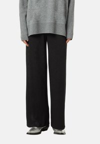 Pull en tricot gris oversize avec des poignets côtelés, associé à un pantalon large noir pailleté et des bottes argentées.