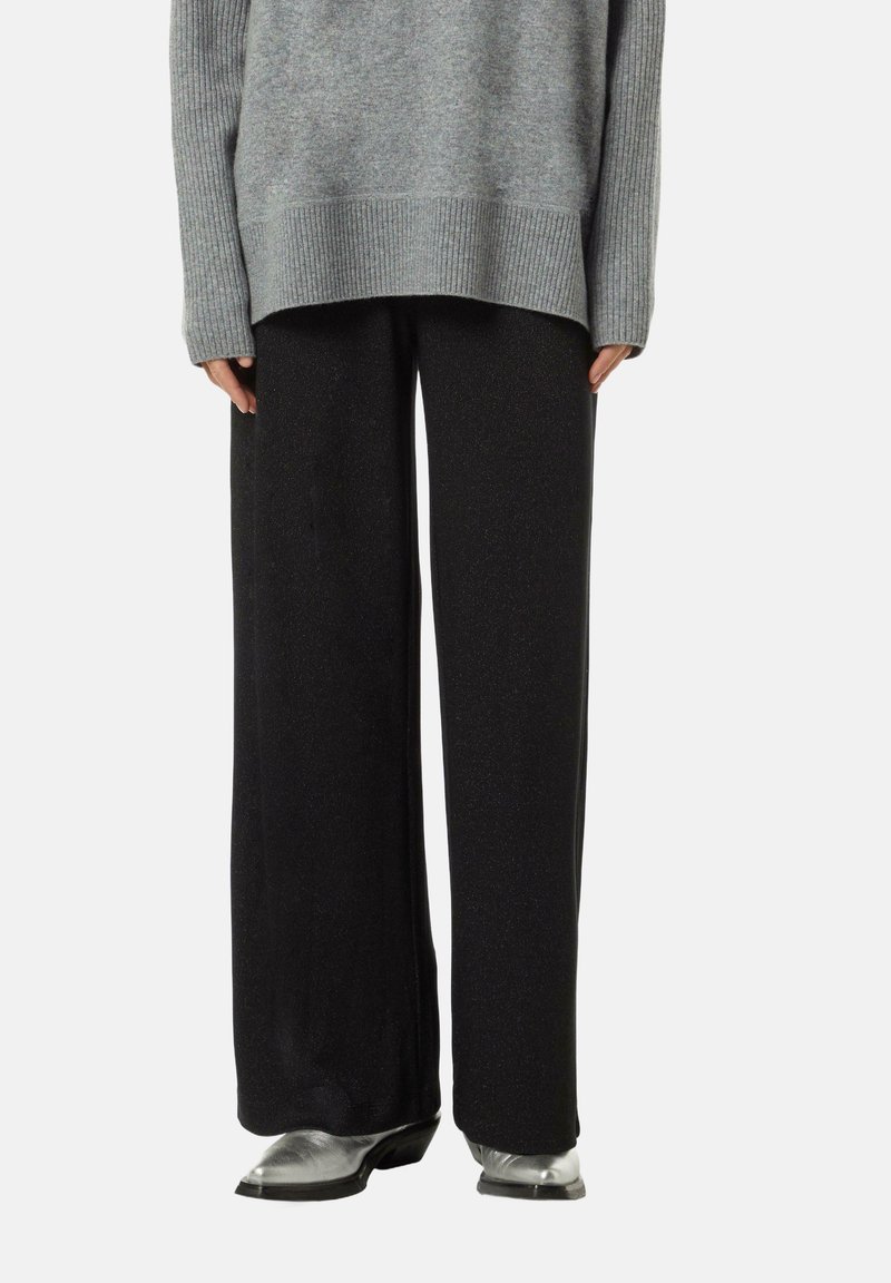 Pull en tricot gris oversize avec des poignets côtelés, associé à un pantalon large noir pailleté et des bottes argentées.