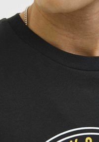 Camiseta de algodón negra con cuello redondo y una textura suave, que presenta un diseño gráfico amarillo y blanco en el frontal.